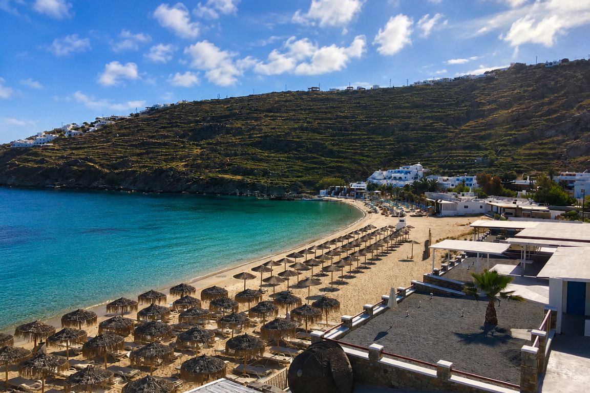 Panoramic view of Psarou Beach in Mykonos with turquoise waters, beach umbrellas, and seaside resorts visited during a Mykonos Tours excursion